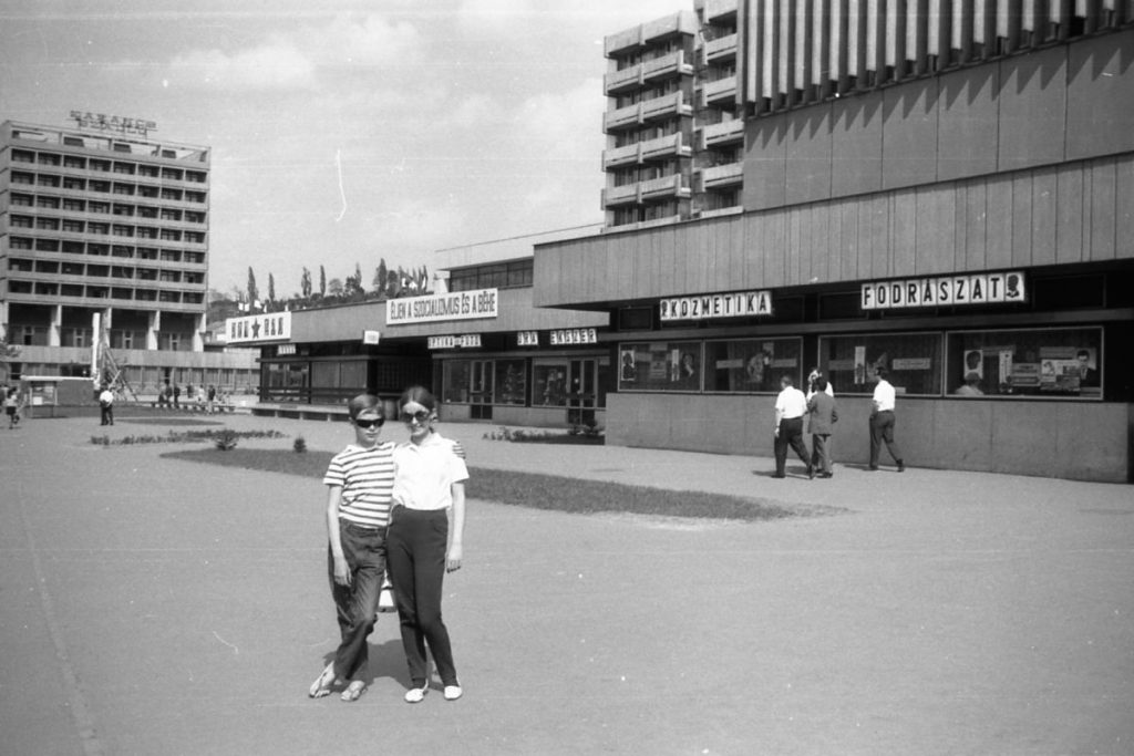 A Pécskő Üzletházat 1968 áprilisának első napjaiban adták át. A helyi buszállomás 1972 szeptemberének végén költözött el a posta előtti területről, ezt követően létesült a városközponti buszmegálló. A felvétel is ebben az évben készült. Az általunk megkérdezettek nem emlékeztek arra, hogy az idők során cserélték volna az ülő alkalmatosságokat. A padok tehát több mint fél évszázadon keresztül szolgálták a városlakókat, jellemzően a várakozó utasokat. (Fotó: Fortepan / Dunai László)